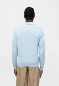 Gaiši zils trikotāžas kardigans ar apkaklīti, garām piedurknēm un ribotu apakšmalu. Gluda tekstūra ar minimālu redzamu detaļu skaitu.