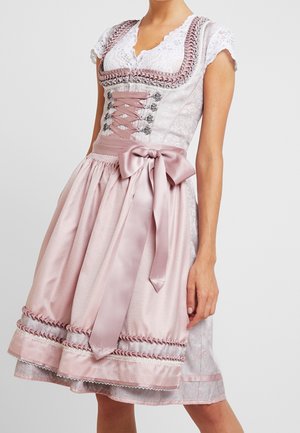 Kvinde iført en pink og hvid traditionel dirndl-kjole med snøreliv, bølget blonderkant, korte ærmer og en stor satin sløjfe i taljen.