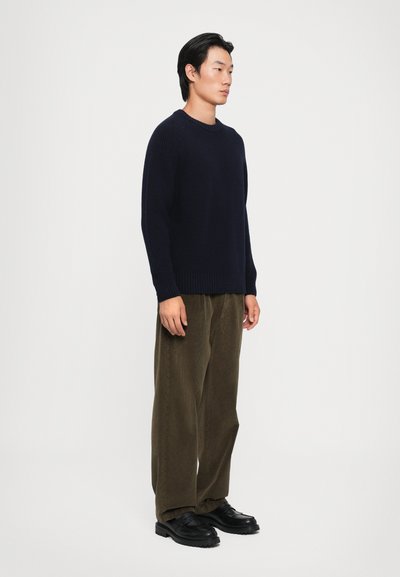 Pulover tricotat navy cu guler rotund, asortat cu pantaloni din corduroy verde măsliniu și pantofi negri texturați. Siluetă simplă, confortabilă.