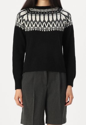 Maglione nero lavorato a maglia con motivo geometrico bianco sul giromanica, colletto rotondo e polsini a costine. Abbinato a pantaloni corti grigi per creare un contrasto.