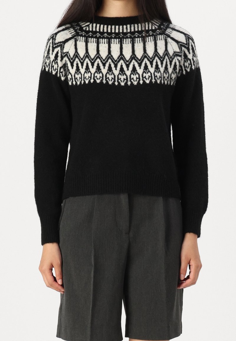 Svart stickad tröja med vitt geometriskt mönster vid oket, rund hals och ribbade muddar. Kombination med grå shorts för kontrast.