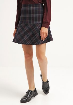 Jupe à carreaux navy avec une taille ajustée et un ourlet évasé. Le tissu a une texture lisse avec des couleurs contrastantes dans le motif. Des chaussures noires complètent le look.