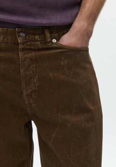 Pantaloni de blugi maro cu finisaj texturat, prevăzuți cu închidere cu nasturi și buzunare laterale. Materialul prezintă modele subtile de uzură.