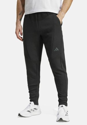 Zwarte sportieve broek met een taps toelopend ontwerp, voorzien van zijzakken en een subtiele drie-streep logo op de linker dij. Gemaakt van een zachte stof.