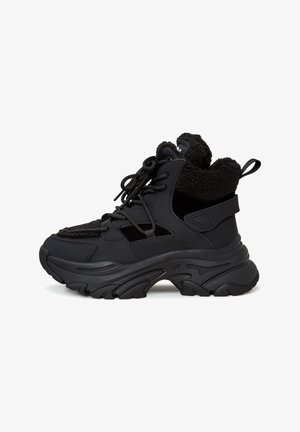 Baskets montantes noires alliant cuir lisse et tissu texturé, dotées d'une semelle épaisse et d'un système de laçage.