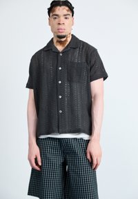 Svart strikket kortermet skjorte med lomme og knappelukking, kombinert med rutete shorts i mørkegrønn og svart.