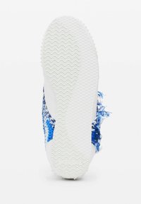 Suola di sneakers bianche con un motivo a onde testurizzato, circondata da una tomaia intrecciata blu e bianca con accenti sfilacciati.