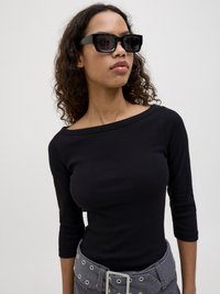 Black ribbed long-sleeve top with a wide neckline, paired with gray high-waisted pants featuring grommet details and a rectangular buckle.