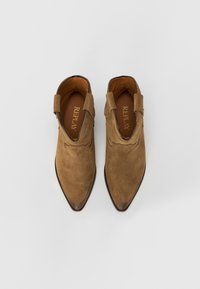 Bottes de cheville en daim beige avec des bouts pointus, une texture douce et des accents latéraux en boucle. Logo "REPLAY" visible sur les semelles intérieures.