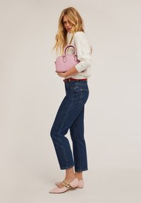 Roze handtas met dubbele handvatten, gecombineerd met een witte trui, donkerblauwe straight-leg jeans en lichtroze puntige ballerina's met gouden accenten.