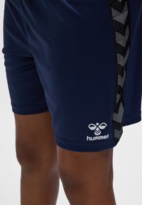 Marineblauwe sportshorts met een gladde textuur, voorzien van een zwart patroon aan de zijkant en een wit logo op de zoom.