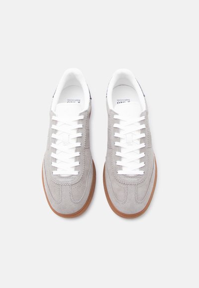 Ζευγάρι ανοιχτόχρωμων γκρι σουέντ αθλητικών παπουτσιών με λευκά κορδόνια και καφέ λαστιχένιες σόλες, φωτογραφημένα από πάνω σε λευκό φόντο.