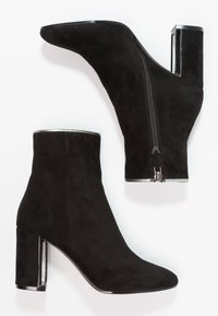 Black suede ankle boots with a pointed toe, sleek silhouette, and a square heel featuring a metallic accent and side zipper.