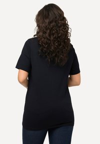 Camiseta negra de manga corta exhibida desde atrás. Fabricada con una tela suave, tiene un corte holgado y un dobladillo curvado. Se lleva con jeans azules.