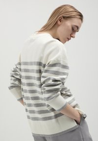 Cremfarbener und grauer gestreifter Pullover mit lockerer Passform, langen Ärmeln und gerippten Bündchen. Besitzt einen weiten Kragen und seitliche Schlitze am Saum.