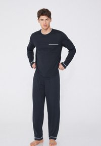 Conjunto de pijama azul marino que incluye una camiseta de manga larga con ribete y bolsillo blancos, acompañada de pantalones a juego. Tela suave.