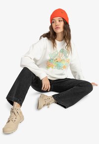 White sweatshirt with colorful graphic, black wide-leg jeans, and beige lace-up boots. Bright orange ribbed knit beanie worn.