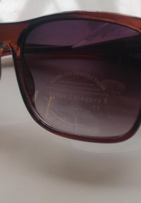 Hnědé sluneční brýle s tónovanými skly a tmavě fialovými čočkami, na vnitřní straně skel s označením "Úplná UV ochrana" a "Kategorii filtru 2".