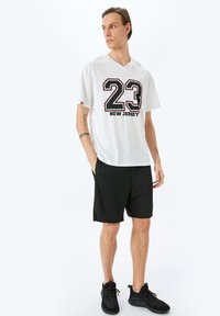 Hvid kortærmet t-shirt med sort "23" og "NEW JERSEY" print, parret med sorte atletikshorts og sorte sneakers.