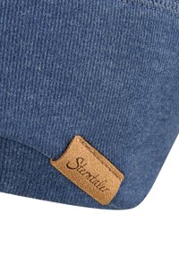 Blue ribbed fabric close-up with a small tan leather tag stitched on, featuring the word "Stentaller" embossed in cursive.