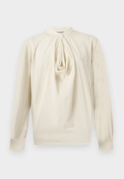 Blouse crème à manches longues avec détail plissé en forme de trou-de-serrure sur le devant et col montant, fermeture par bouton au niveau du cou et manches avec poignets.