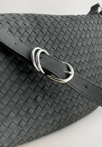 Schwarze gewebte Handtasche aus strukturiertem Material mit einem glatten Riemen, silbernen Metallakzenten und einem einzigartigen verflochtenen Design.