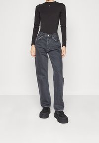 Maglia nera a maniche lunghe abbinata a jeans grigi a vita alta e fit comodo. I jeans presentano un classico design a cinque tasche e un orlo sfrangiato. Scarpe nere con plateau.