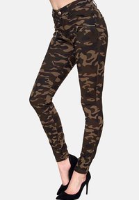 Camouflage-musterte Skinny Jeans in dunklen Grüntönen und Brauntönen, mit Reißverschlusstaschen und einer schmalen Passform. Der Stoff hat eine glatte, dehnbare Textur.
