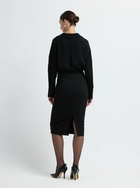 Svart blus med ett subtilt mönster, instoppad i en figurnära svart blyertskjol med en slits bak, i kombination med svarta högklackade skor.