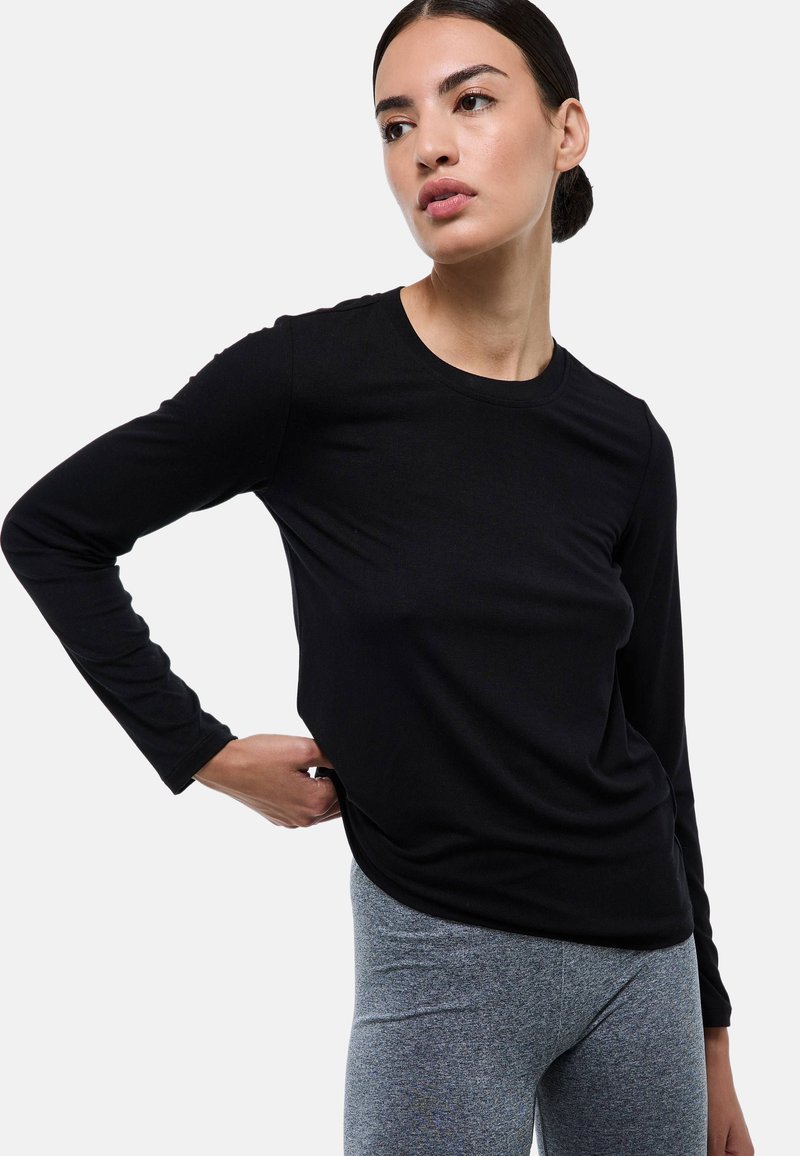 Haut noir à manches longues en tissu côtelé, avec un col rond et une coupe décontractée, associé à des leggings texturés gris.