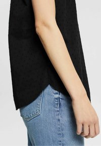 Haut noir texturé avec un ourlet festonné, associé à un jean en denim bleu clair. Le tissu présente de petits points en relief pour un détail supplémentaire.