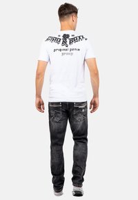 T-shirt bianco a maniche corte con stampa grafica nera sul retro, abbinato a jeans in denim nero con cuciture decorative e tasche.