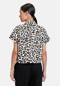 Cropped short-sleeve shirt featuring a leopard print in black and tan on a white background, with a classic collar and smooth fabric texture.