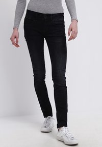 Jeans negros ajustados con un ligero deslavado, diseño de cinco bolsillos y cintura a media altura, combinados con zapatillas blancas y una camiseta gris con relieve.