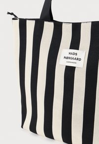 Torebka na ramię w czarno-kremowe paski wykonana z trwałego materiału, z metką "MADS NORGAARD COPENHAGEN". Solidny uchwyt na górze.