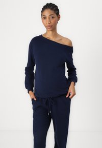 Felpa blu navy, senza spalle, con maniche lunghe e polsini a costine, abbinata a pantaloni sportivi con cordino coordinati. Tessuto morbido.