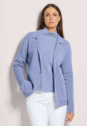 Cardigan tricoté bleu clair avec un design structuré, à l'avant ouvert, et deux poches avant. Texture côtelée sur les manches et un pull à col montant en dessous.