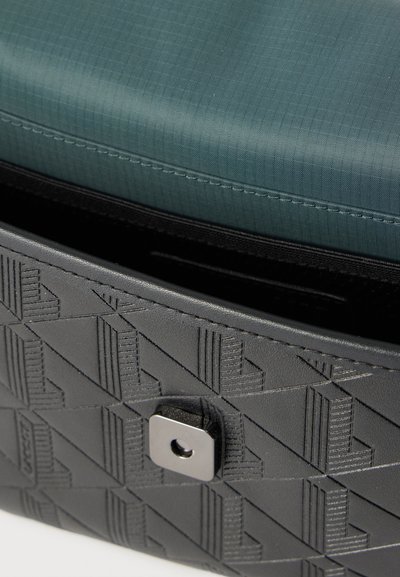 Sac à main en cuir noir embossé avec motif géométrique et fermeture métallique, partiellement ouvert pour révéler une doublure en tissu bleu à l'intérieur.