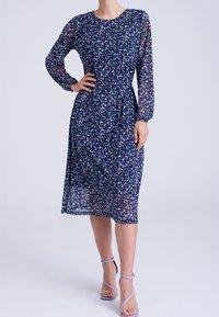 Mekko, jossa on kukkakuvio, tummansinistä läpikuultavaa kangasta, pitkät hihat ja kootut vyötärö. Mukana vaaleanpunaisia ja valkoisia pieniä kukkia sekä lentävä siluetti.