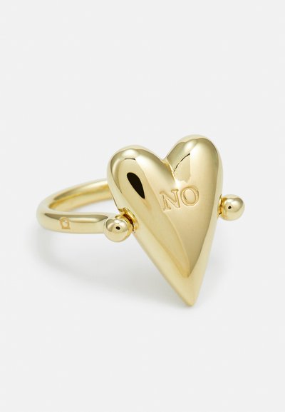 Gold farbener, herzförmiger Ring mit einer glatten Oberfläche, der auf einer Seite das Wort "NEIN" eingraviert hat und kleine, kugelförmige Akzente am Ringband aufweist.
