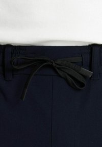 Mornarske hlače s pojasom na vezanje i crnim naglascima, izrađene od glatkog materijala s vidljivim detaljima šivanja.