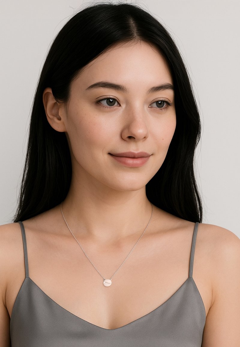 Silver halsband med en rund medaljong, bärs av en modell med mörkt hår. Modellen har på sig en grå satin cami-topp.