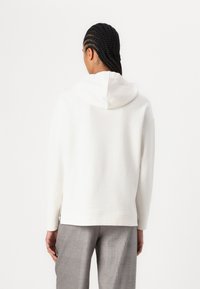 Cremefarbener Hoodie mit einer Kapuze mit Zugband, gerippten Bündchen und Seitenschlitzen. Kombiniert mit grauen gemusterten Hosen. Minimalistisches Design und glatte Textur.