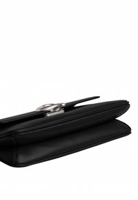 Pochette en cuir noir avec fermoir circulaire argenté, design élégant et coutures visibles le long des bords sur fond blanc.