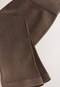 Barna bordázott leggings sima textúrával és testhezálló kialakítással. Az alsó széleket egy szegőpánttal varrták a kényelmes illeszkedés érdekében.