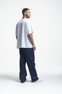 Weißes, oversized Kurzarm-T-Shirt kombiniert mit dunkelblauen, lässigen Jeans, abgerundet mit weißen Sneakern. Minimalistisches Design, ohne Muster.