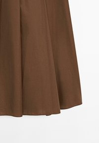 Hnědá sukně po kolena vyrobená z hladké látky, má jednoduchý design s rozšířeným lemem a žádné viditelné ozdoby.