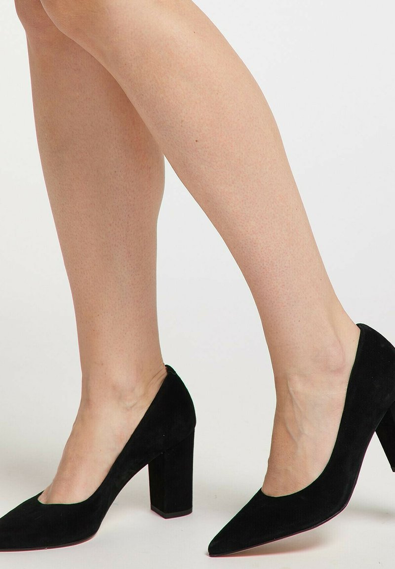 Scarpe nere in suede con tacco alto, caratterizzate da una punta affilata e un tacco spesso. Texture liscia con un design a intaglio lungo i bordi.