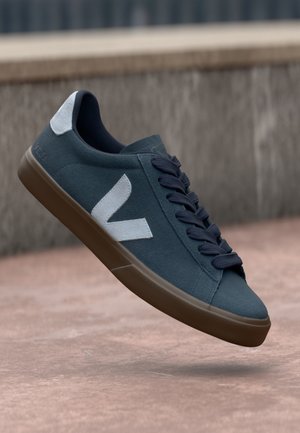 Blue suede sneaker with white logo, round toe, and dark laces. Rubber sole with textured grip. Minimalist design with contrasting accents.