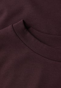 Burgundowa bawełniana tkanina z wykończeniem w prążek; gładka tekstura z subtelnymi detalami haftu i klasycznym okrągłym dekoltem.